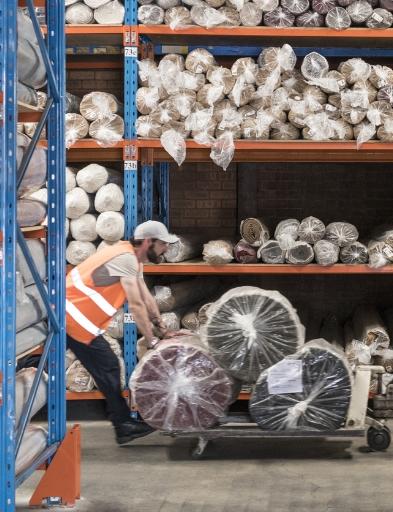 Carpet racks help this warehouse employee find and store rolls of carpet for customers.